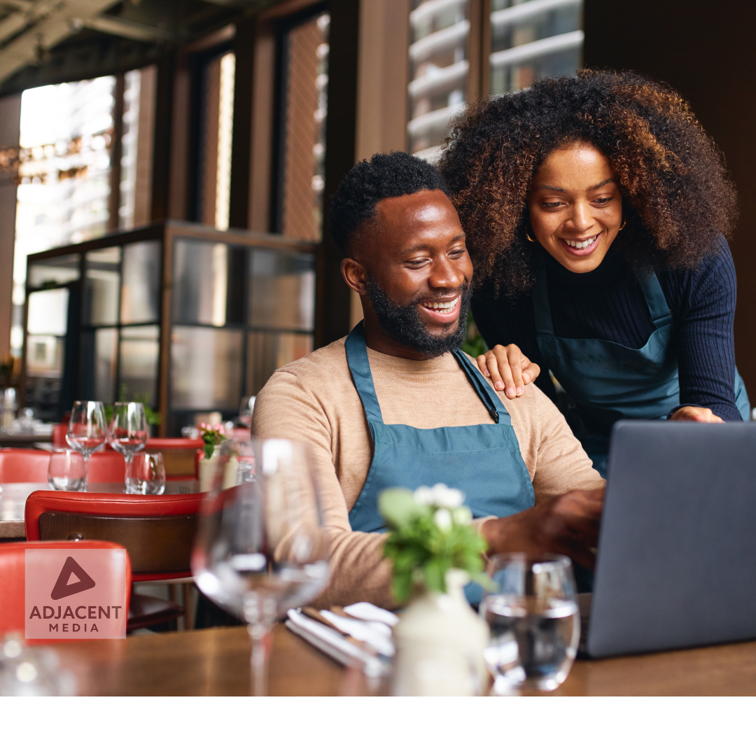 Small business owners smiling and reviewing branding content on a laptop inside a modern restaurant.