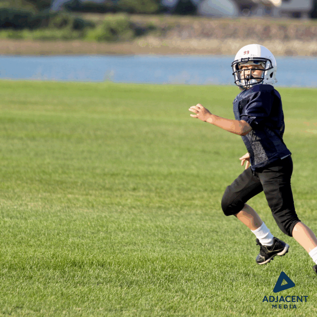 Youth football player in action during a game on a green field, captured mid-play.