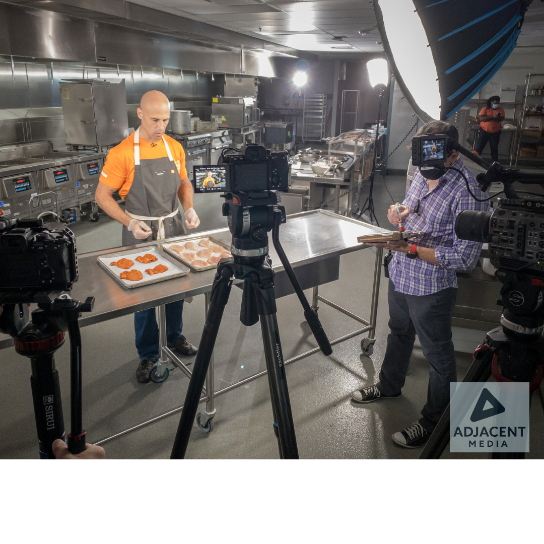 Behind-the-scenes video shoot in a commercial kitchen with a chef and video production crew.