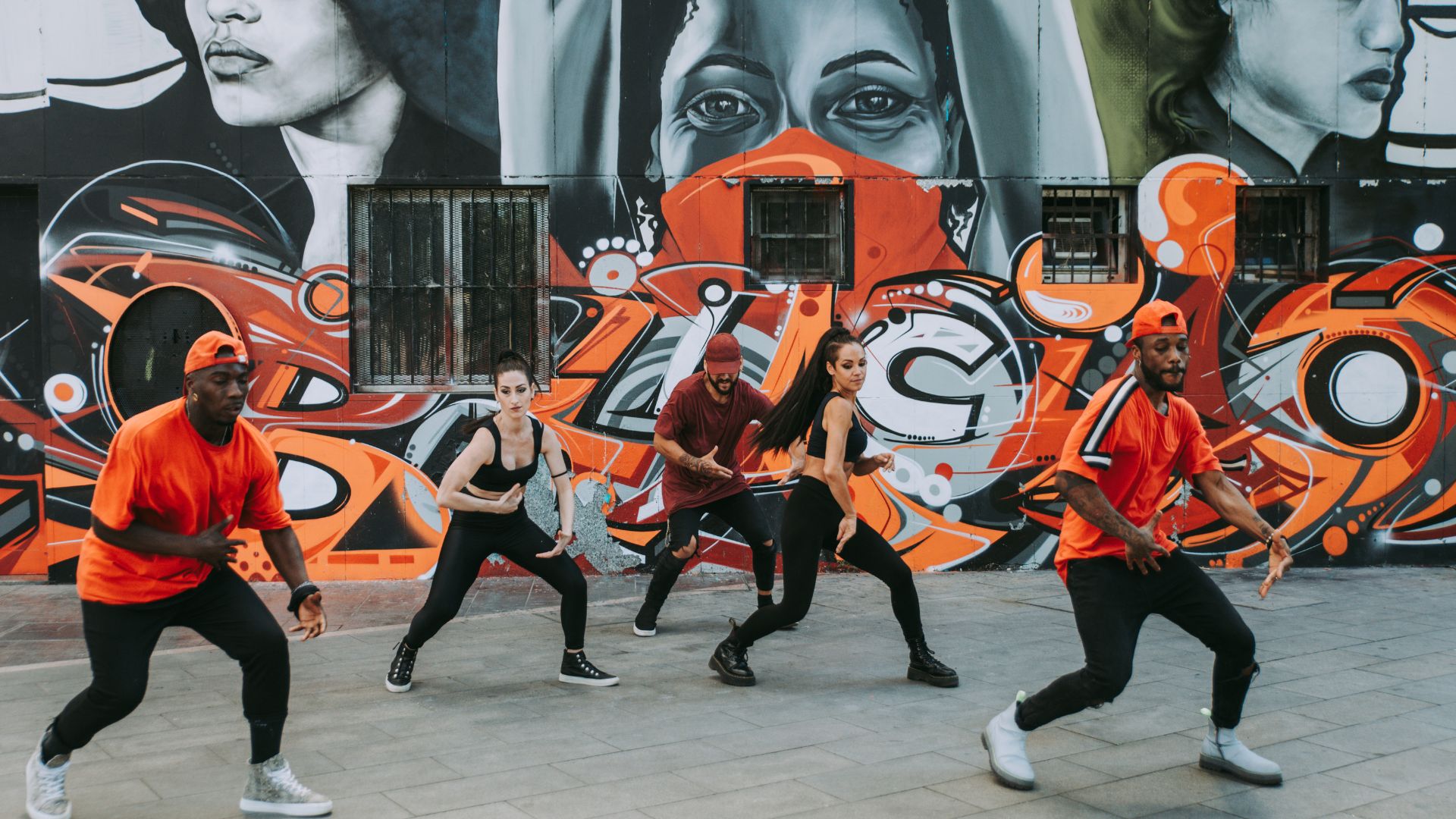 Hip-hop dancers performing in front of a vibrant street art mura